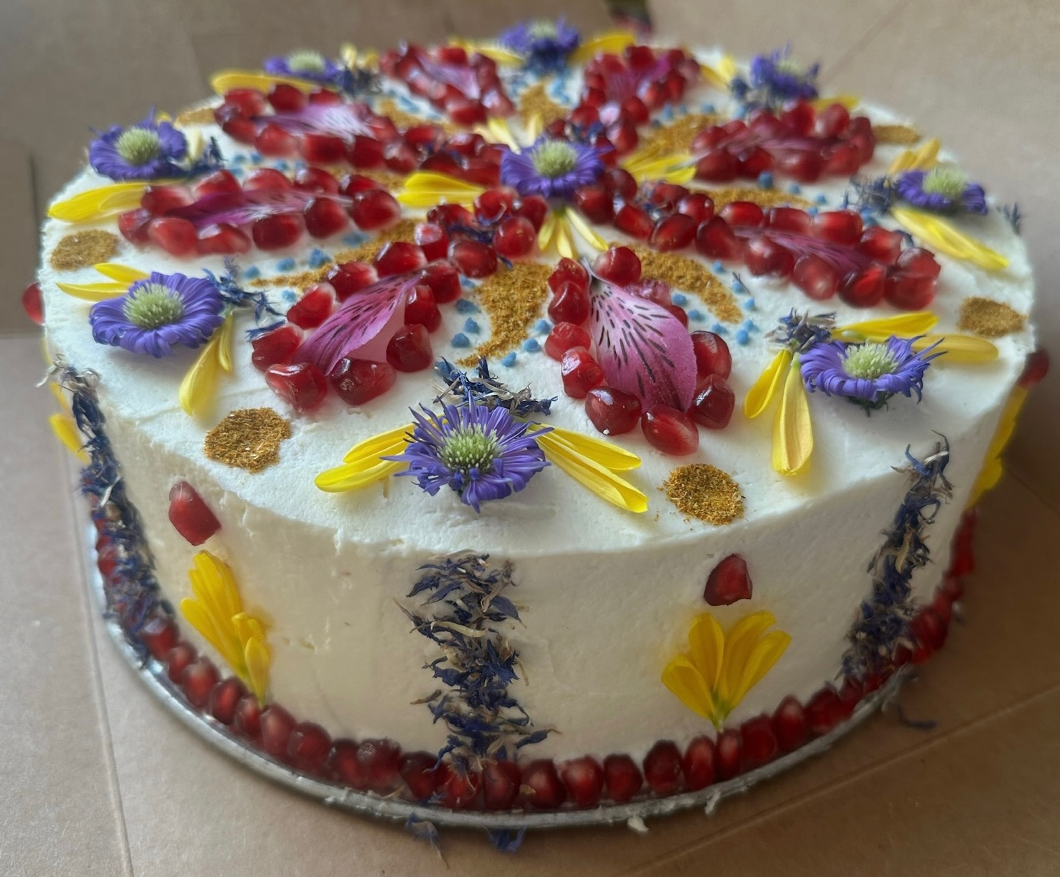 White decorated cake with pomegranate border and purple flowers